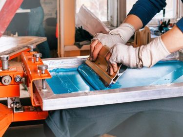 silk screen printmaking. male hands with a squeegee. serigraphy production selective focus photo. printing images on clothes by silk screen method in a design studio